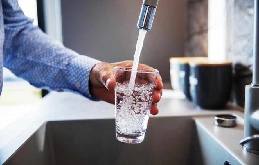 Man in blue dress shirt fills glass with tap water