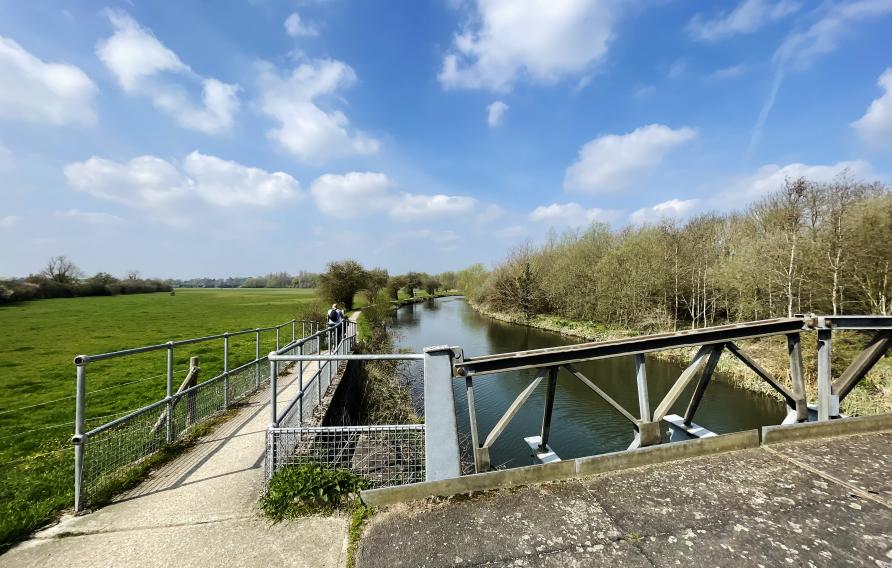 Riverbank and bridge beside a field.