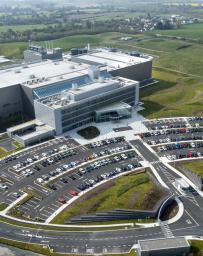 Aerial image of a white office building and parking lot surrounded by green hills