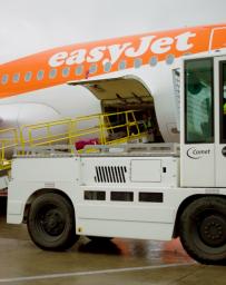 Baggage tractor and luggage cart in front of easyJet aeroplane.